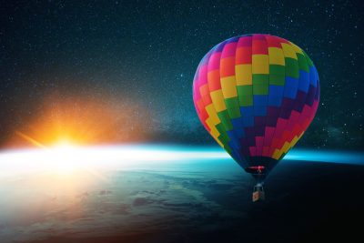 Amazing colored creative air balloon flies in the stratosphere with blue planet earth with sunset against the starry sky background. Space travel and journey concept.